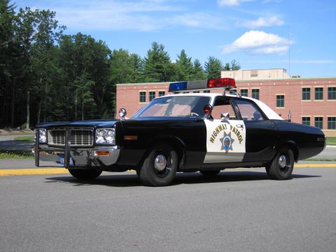 1991 Ford LTD Crown Victoria - black-and-white Highway Patrol police sedan with roof lightbar and push bar parked on a road near woods.
