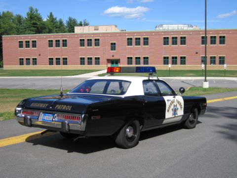 1991 Ford LTD Crown Victoria - Rear three-quarter view of a black-and-white Highway Patrol police sedan parked in front of a two-story brick building.