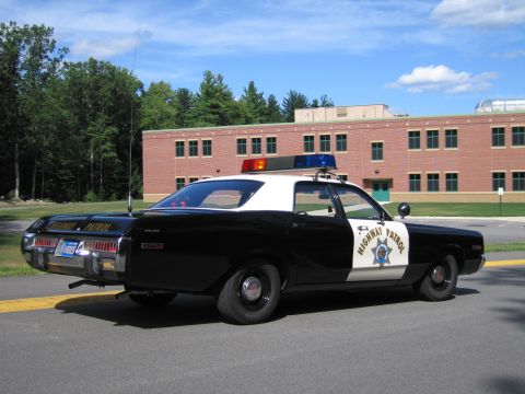 1991 Ford LTD Crown Victoria - Rear side view of a black-and-white Highway Patrol police sedan with roof lightbar parked near a brick building.