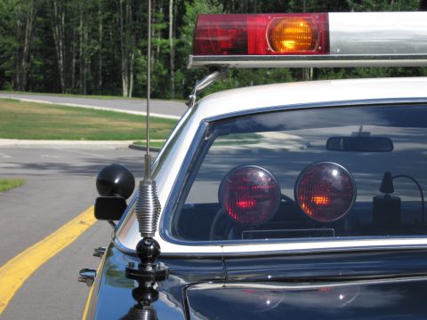 1991 Ford LTD Crown Victoria - Close-up of a police car's roof lightbar, side spotlight, whip antenna and twin red rear-deck warning lights.