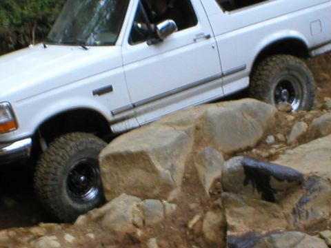1978 Ford Bronco - White SUV carefully maneuvers over a challenging rocky obstacle.