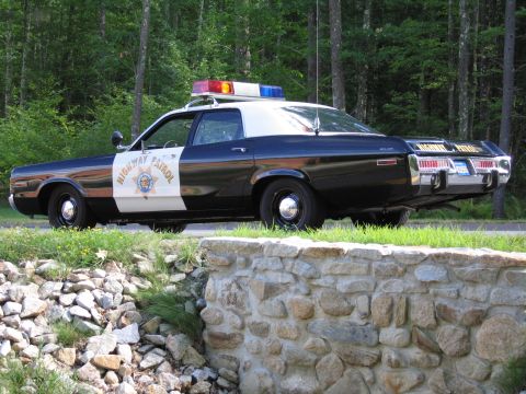 1991 Ford LTD Crown Victoria - Driver-side profile of a black-and-white Highway Patrol police sedan with a star door emblem and roof lightbar, parked by a stone wall and…