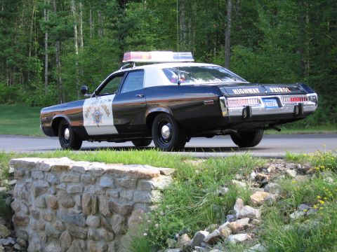 1991 Ford LTD Crown Victoria - Rear three-quarter view of a black-and-white Highway Patrol police sedan with roof lightbar and chrome bumpers, parked along a wooded road.