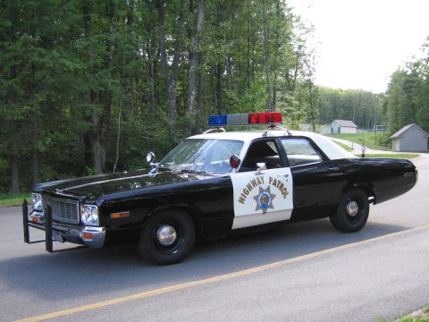 1991 Ford LTD Crown Victoria - black-and-white Highway Patrol police sedan with chrome grille and roof lightbar parked on a paved road with houses and trees behind.