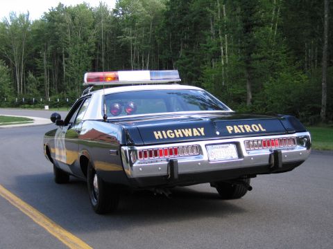 1991 Ford LTD Crown Victoria - Rear view of a dark police sedan with HIGHWAY PATROL lettered across the trunk, dual taillights, chrome bumper and an amber roof beacon lit.