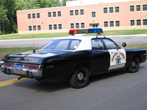 1991 Ford LTD Crown Victoria - black-and-white Highway Patrol police sedan with roof lightbar parked on pavement in front of a long red-brick building.