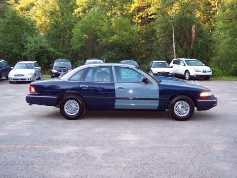 1991 Ford LTD Crown Victoria - Driver-side profile of a two-tone dark-blue and gray Ford sedan parked in a gravel lot with other vehicles and trees behind.