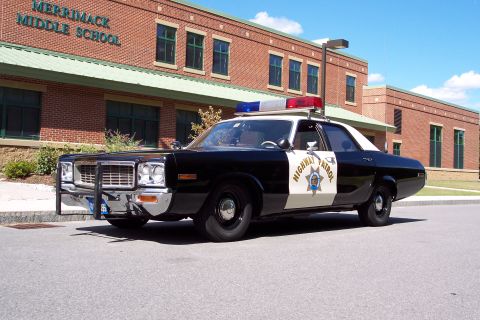 1991 Ford LTD Crown Victoria - black-and-white Highway Patrol sedan with chrome push bar and roof light bar sits outside Merrimack Middle School under a blue sky.