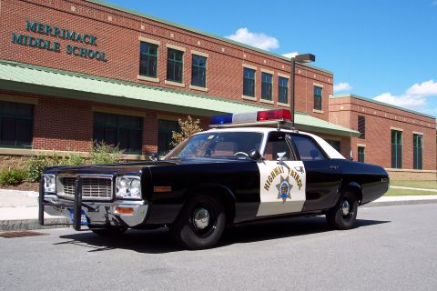 1991 Ford LTD Crown Victoria - Front three-quarter view of a black-and-white Highway Patrol sedan with push bar and light bar parked outside a brick middle school.
