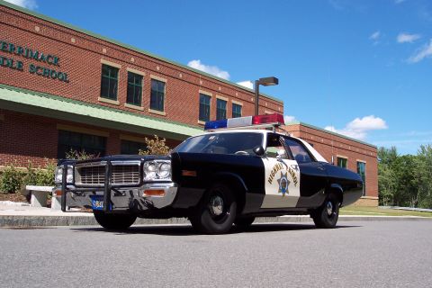 1991 Ford LTD Crown Victoria - low front-angle view of a black-and-white Highway Patrol sedan with chrome push bar and door star decal outside a brick school.