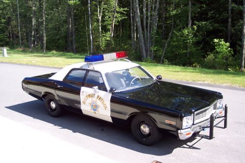 1991 Ford LTD Crown Victoria - Front three-quarter view of a black-and-white Highway Patrol sedan with chrome push bar and roof light bar on pavement before green woods.
