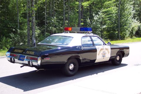1991 Ford LTD Crown Victoria - Rear three-quarter view of a black-and-white Highway Patrol sedan with 'HIGHWAY PATROL' lettering on the trunk and roof light bar lit amber.