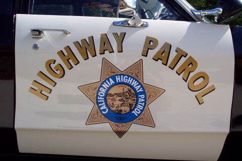 1991 Ford LTD Crown Victoria - Close-up of a white car door painted 'HIGHWAY PATROL' in gold lettering around the California Highway Patrol seven-point star seal.
