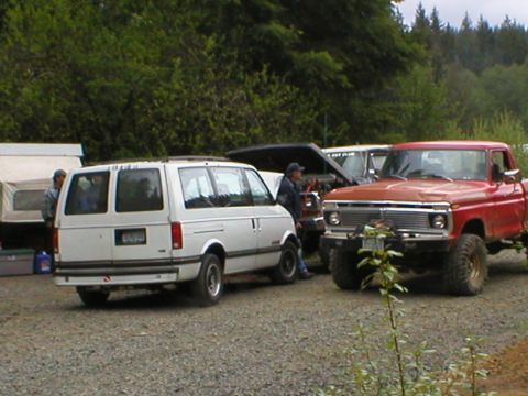 1978 Ford Bronco - A red 1975 Ford F-Series pickup truck is parked next to a white van, with trees in the background.