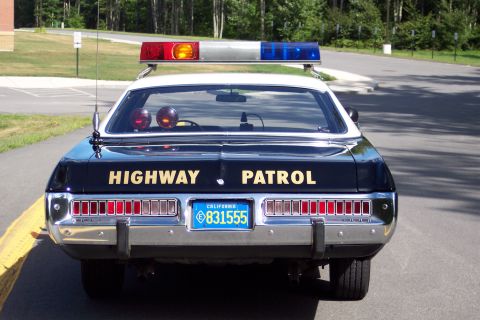 1991 Ford LTD Crown Victoria - Direct rear view of a black patrol sedan with gold HIGHWAY PATROL lettering, roof lightbar, and California plate 831555.