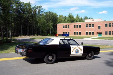 1991 Ford LTD Crown Victoria - Rear-side view of a black-and-white California Highway Patrol sedan with door star and roof lightbar, brick building behind.