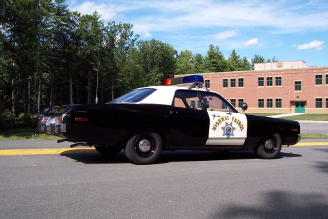 1991 Ford LTD Crown Victoria - Side-rear view of a black-and-white California Highway Patrol sedan with door star emblem and roof emergency lights near a brick building.