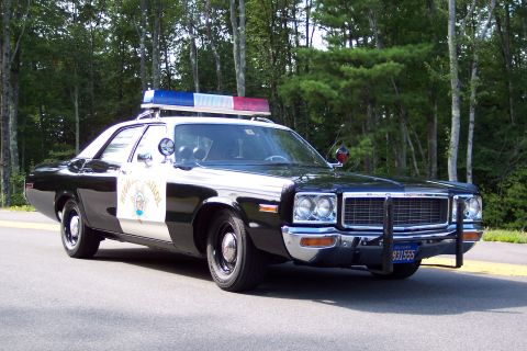 1991 Ford LTD Crown Victoria - Front-side view of a black-and-white California Highway Patrol sedan with chrome push bumper, door star emblem, and roof lightbar by trees.
