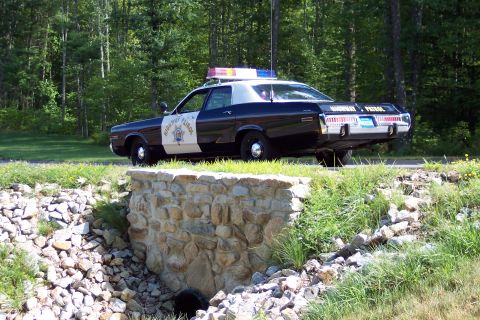 1991 Ford LTD Crown Victoria - black-and-white Highway Patrol cruiser with rooftop lights and Highway Patrol door lettering sits on grass above a stone retaining wall.