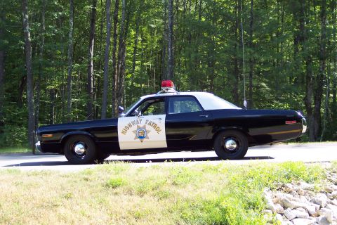 1991 Ford LTD Crown Victoria - Full side profile of a black-and-white Highway Patrol cruiser with roof light and Highway Patrol door lettering, parked along a green woode…
