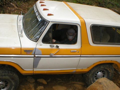 1978 Ford Bronco - A driver in a cap is visible through the window of a classic 1978 Ford Bronco parked on rocky terrain.