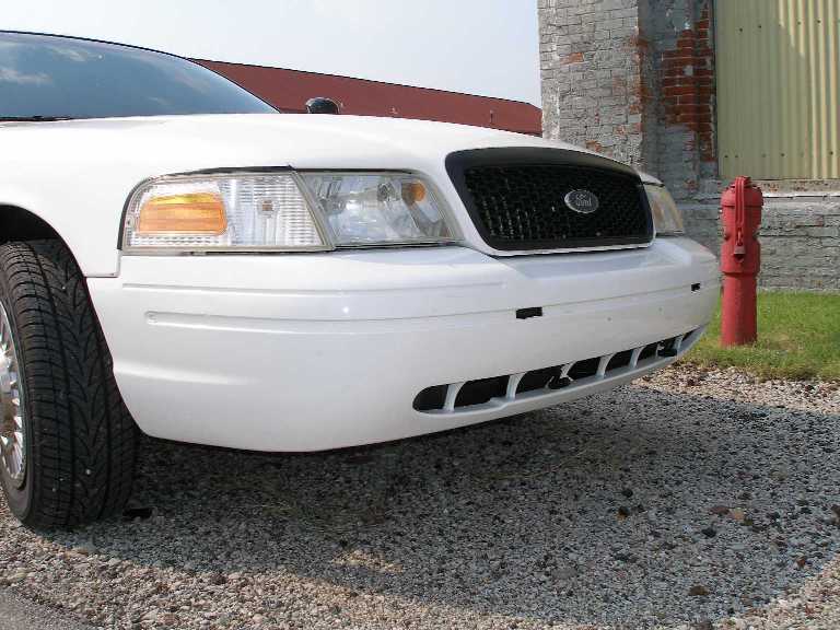 White 2001 Ford Crown Victoria front end with black grille and headlights. Tire visible on left