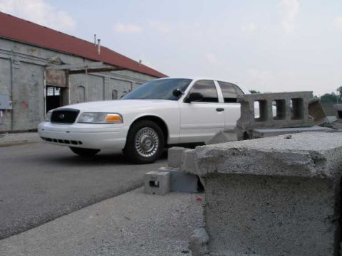 2001 Ford Crown Victoria - White 2001 Ford Crown Victoria parked outside a warehouse with cinder blocks in the foreground.