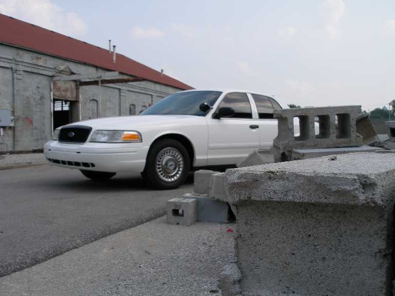 White Ford Crown Victoria shot past broken concrete blocks at an old warehouse
