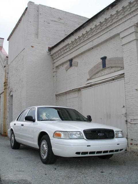 2001 Ford Crown Victoria - A white 2001 Ford Crown Victoria is parked in an alleyway with white brick buildings on either side.