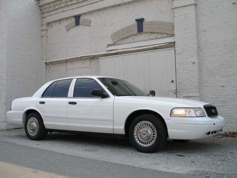 2001 Ford Crown Victoria - A white 2001 Ford Crown Victoria is parked outside a warehouse, showing its front-right side.