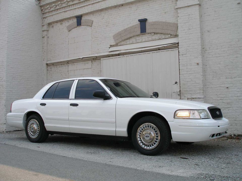 White 2001 Ford Crown Victoria parked on asphalt in front of a white brick building with a large garage door