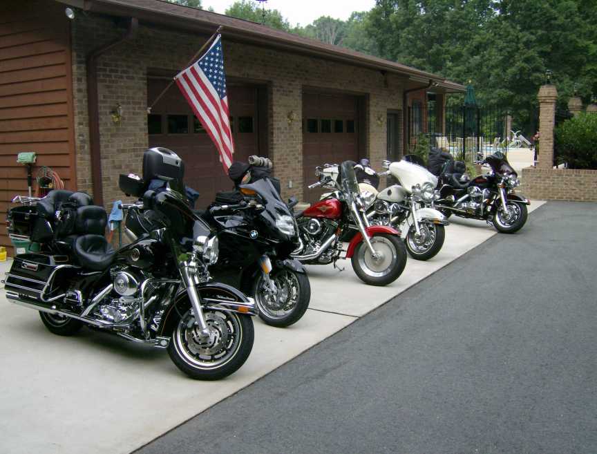 Several motorcycles are parked in a driveway in front of a brick garage with an American flag flying