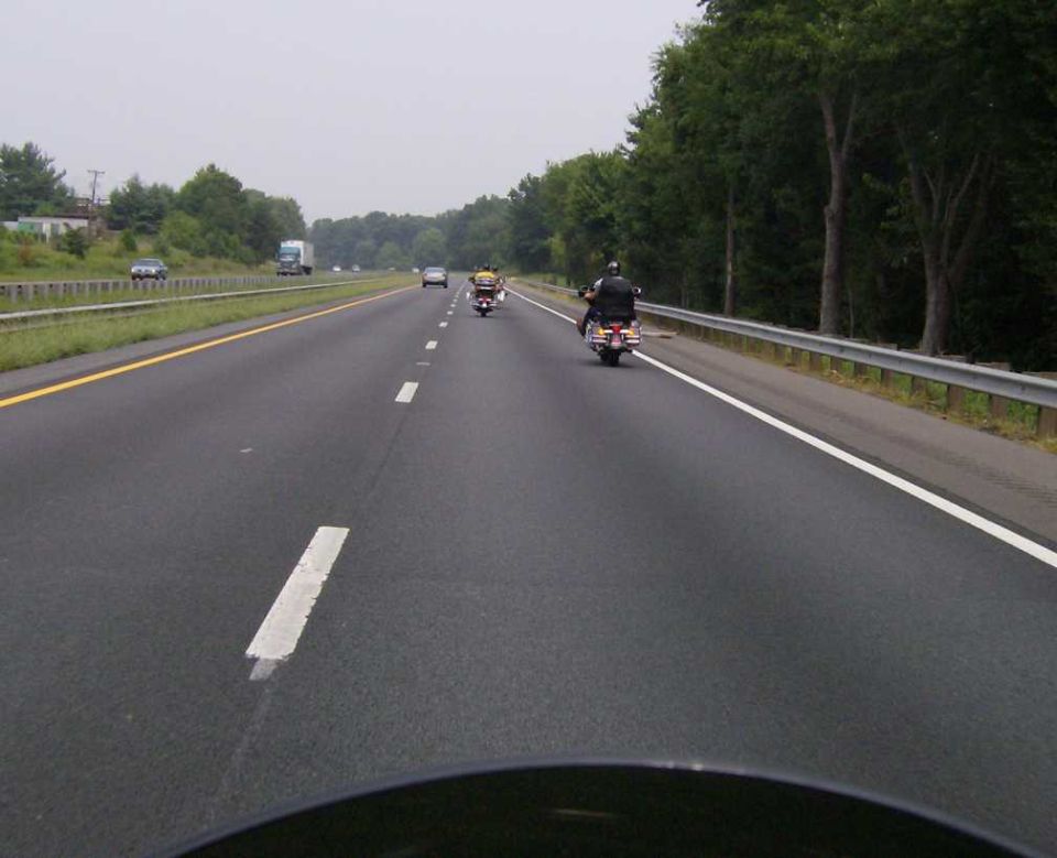 Motorcycles on a highway, with trees and a guardrail on the right