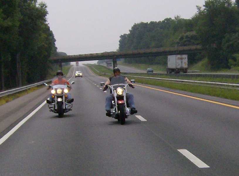 Two motorcycles riding on a highway under an overpass
