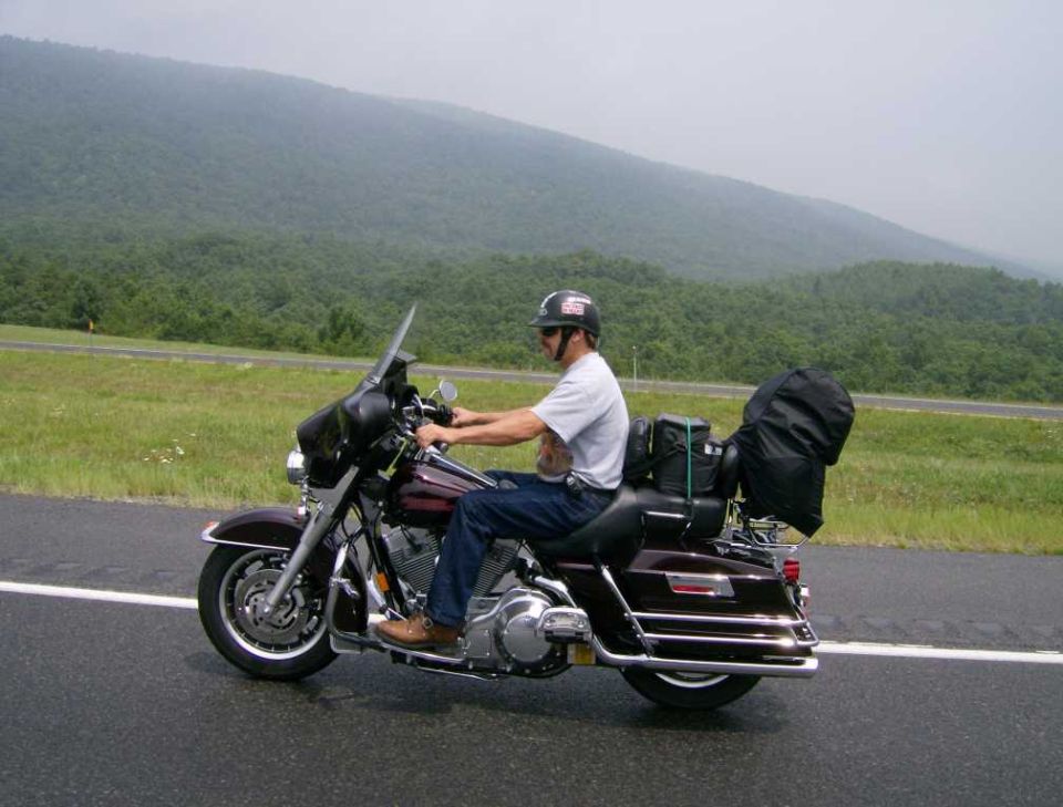 Man riding a motorcycle on a wet road with mountains in the background