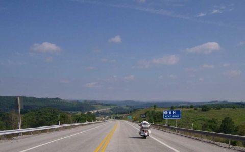 2005 BMW R1200CA ABS - A lone motorcycle travels down a highway with rolling hills in the background under a partly cloudy sky.