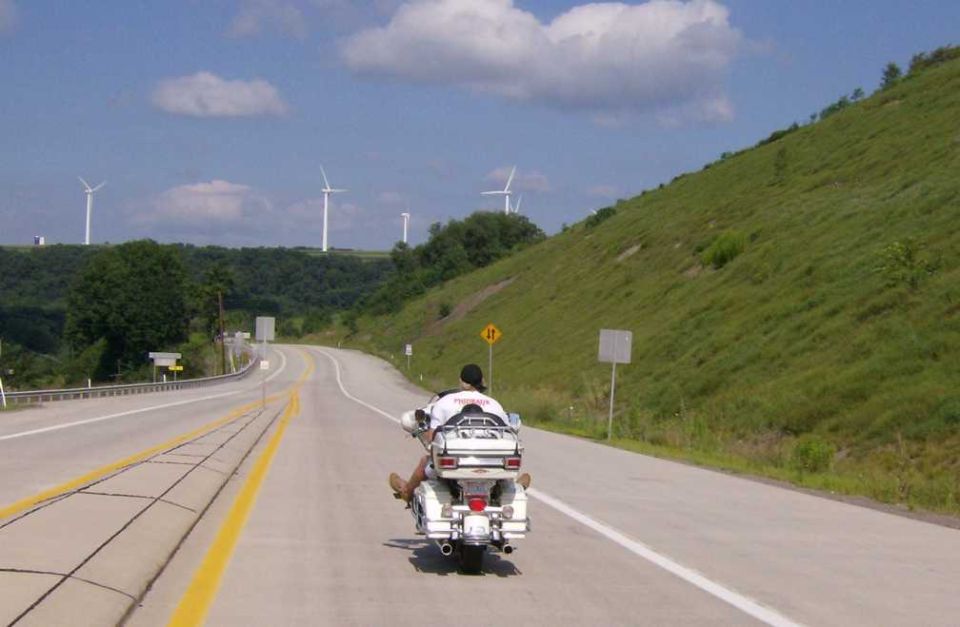 Motorcycle riding on a highway with wind turbines in the background
