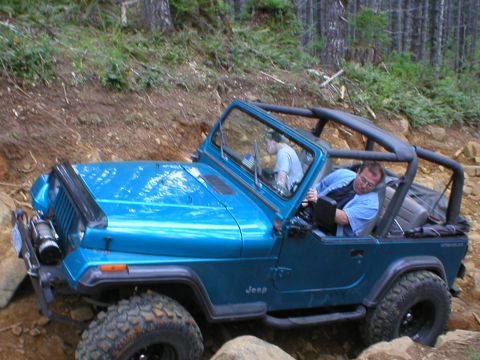 1978 Ford Bronco - A blue Jeep Wrangler navigates a rocky, wooded trail during an off-road excursion.