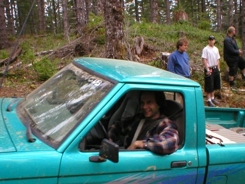1978 Ford Bronco - Man smiles from the driver's seat of a teal pickup truck in a forest setting.