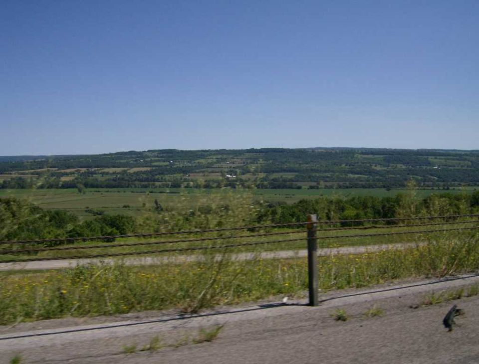 Motorcycle parked on a paved surface with a rural landscape in the background under a clear blue sky