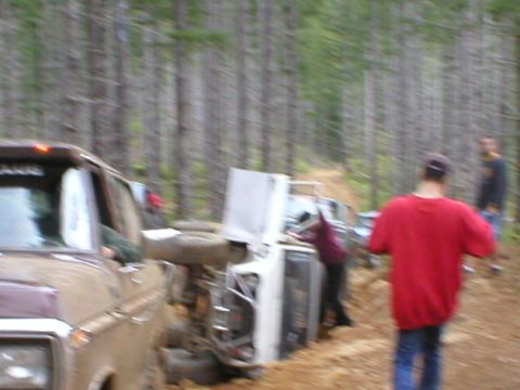 1978 Ford Bronco - Two vehicles are overturned in a wooded area, with two individuals observing the scene.