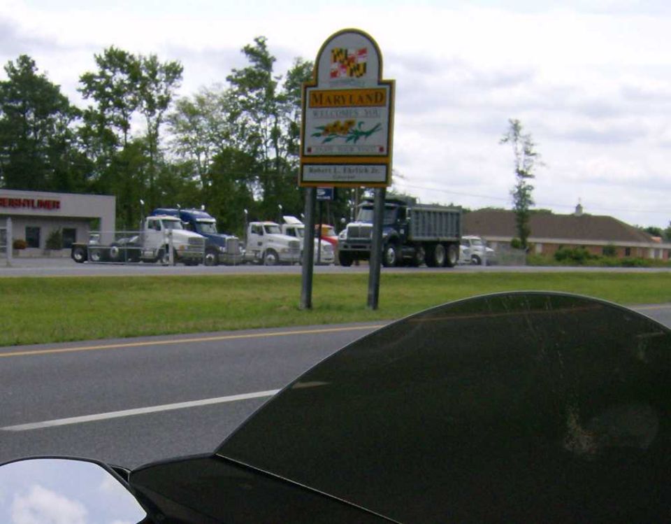 Several semi-trucks parked in front of a Freightliner dealership, with a Maryland welcome sign
