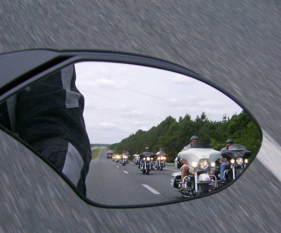 Motorcycle convoy reflected in a side mirror, showing multiple cruisers on a highway