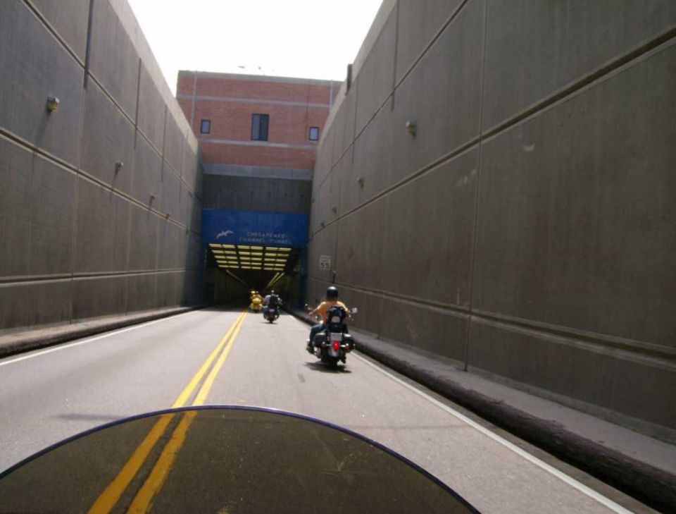 Motorcycles ride through a tunnel with a sign for the Chesapeake Channel Tunnel