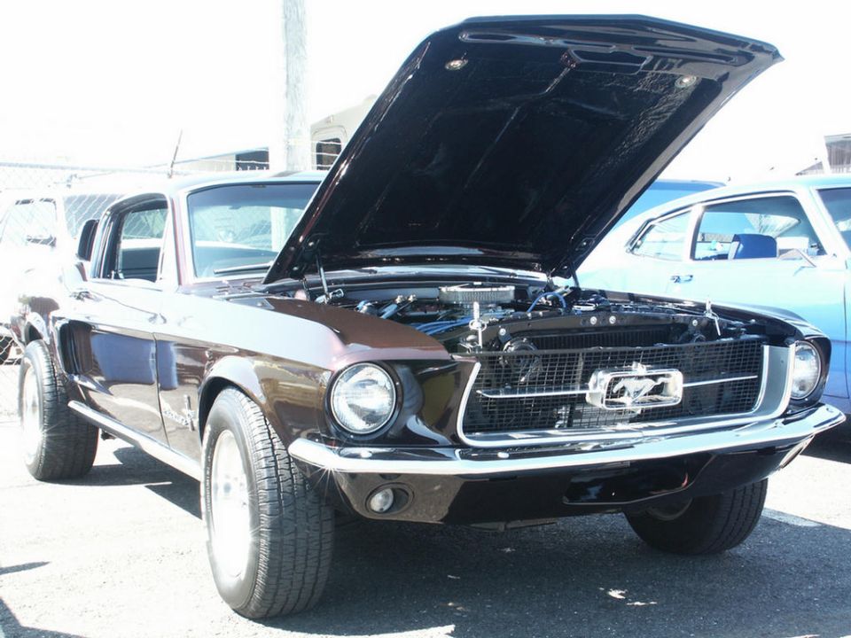 Front view of a brown 1967-1968 Ford Mustang with hood open, showing engine. Another car is parked next to it