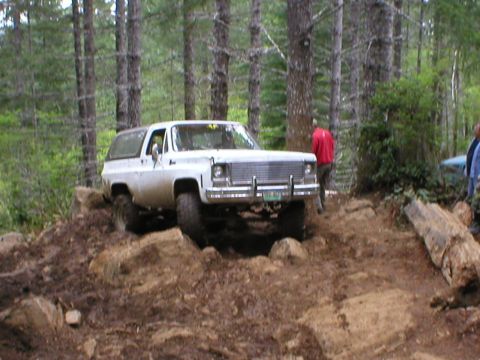 1978 Ford Bronco - A white SUV tackles a rocky, wooded terrain during an off-road excursion.