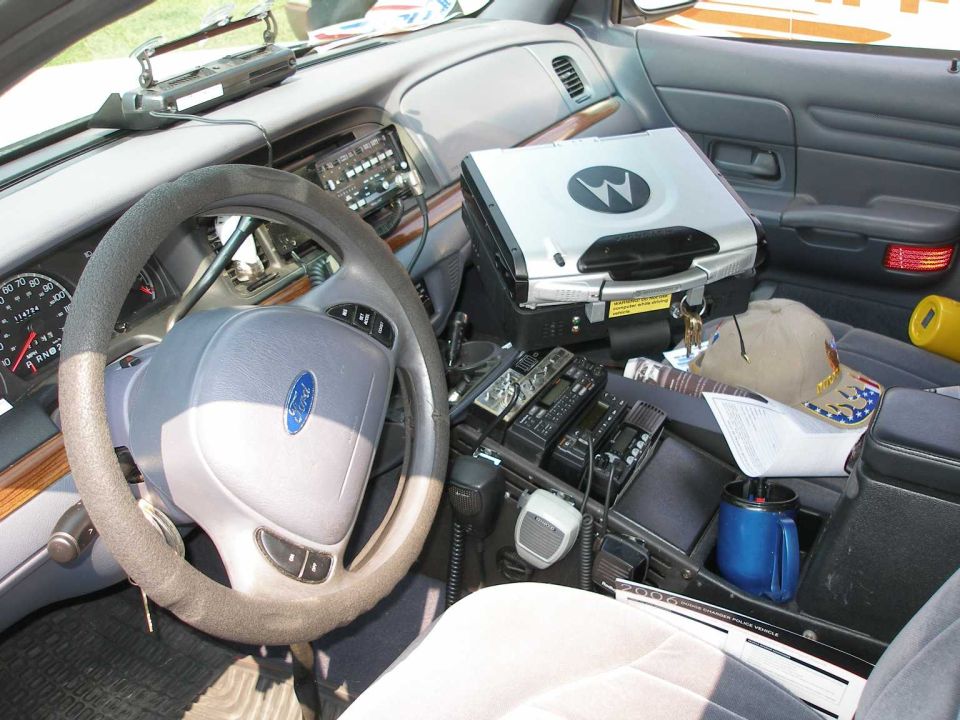 Police car interior with Ford steering wheel, radios, and mounted rugged laptop
