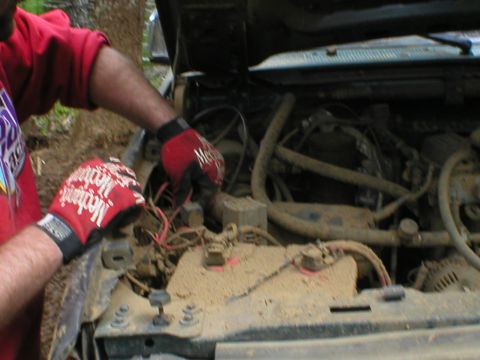 1978 Ford Bronco - Close-up of an engine bay where someone in red mechanic gloves is working on the wiring.