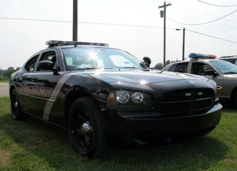 1998 Ford Crown Victoria - A black Dodge Charger police car is parked on grass next to another police vehicle.