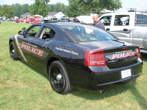 1998 Ford Crown Victoria - A black police car is parked on grass next to a white pickup truck at an outdoor event.